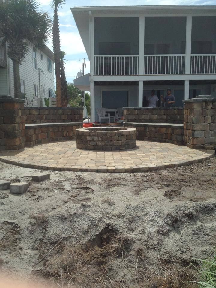 Brick patio with fire pit, stone seating, and a beachfront house.