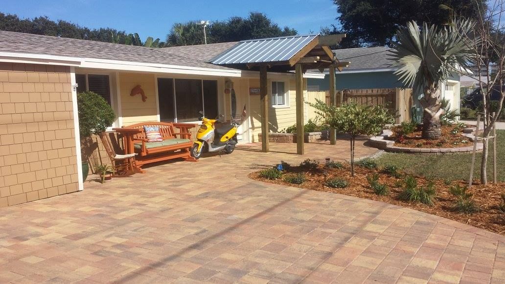 A yellow house with a brick paved driveway, bench, and scooter.