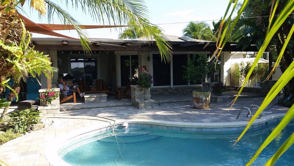 Poolside patio with house, featuring pool, seating, and tropical foliage.