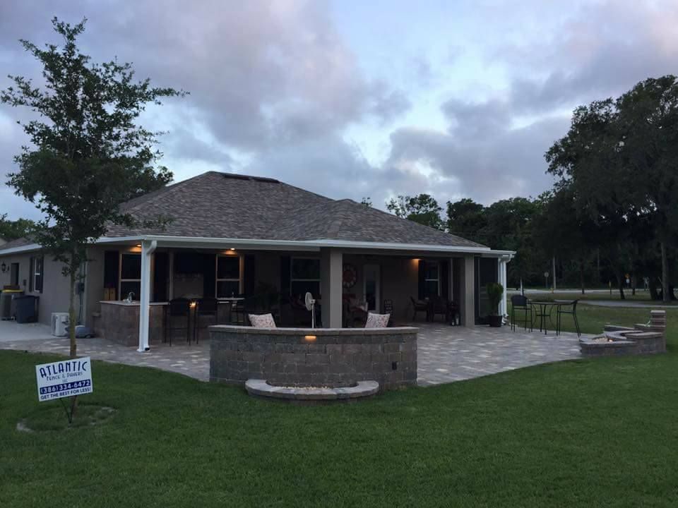 Patio with brick fire pit and house under a cloudy sky.