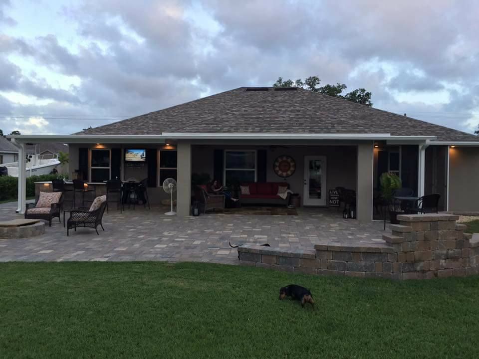 Backyard patio with brick pavers, outdoor furniture, and a fire pit. A dog is in the grass.