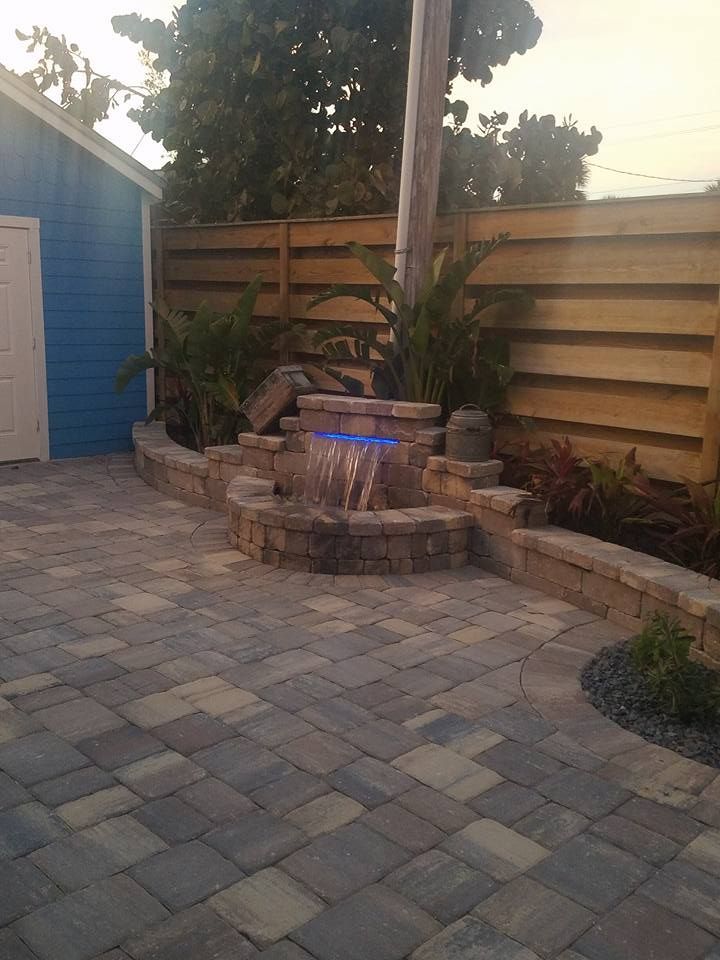 Brick patio with a water feature, blue shed, and wooden fence.