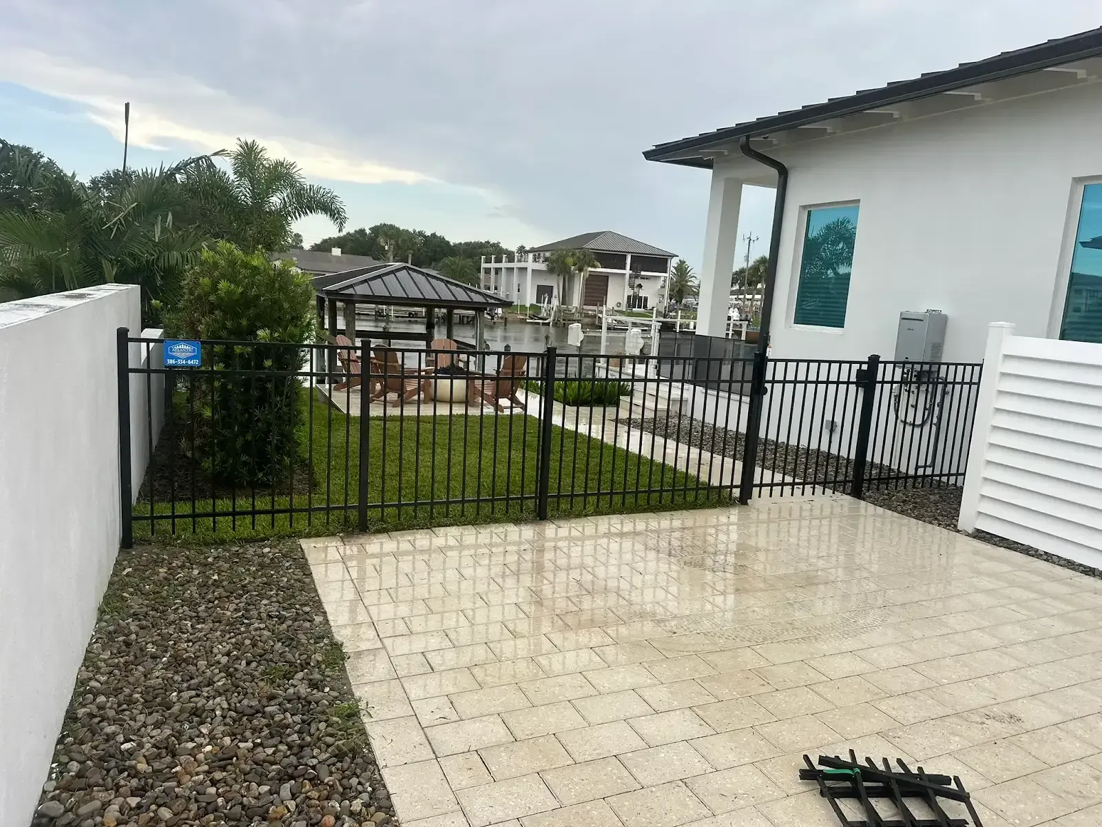 Black metal fence surrounds a patio with pavers and gravel, with a gazebo and water view in the background.