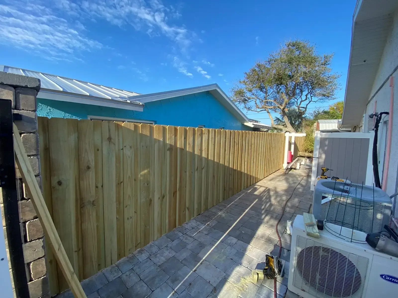 Wooden fence beside a building, pathway between; blue sky, sunny day.