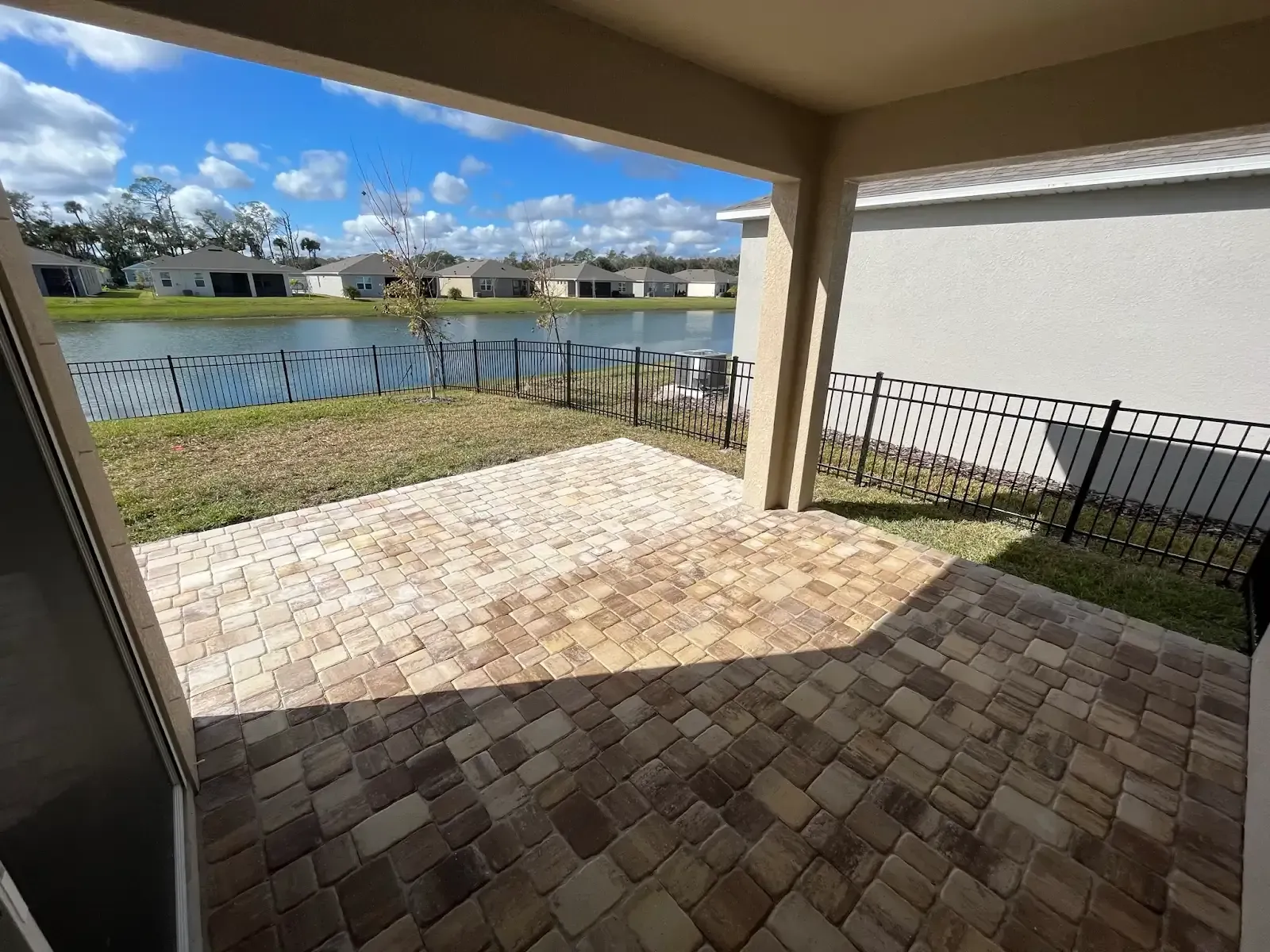 Patio with brick pavers, overlooking a lake and houses under a partly cloudy sky.