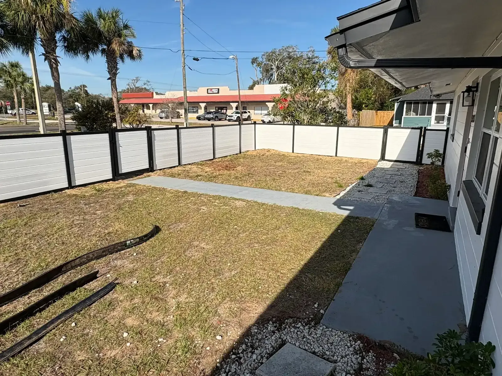 Front yard with a white and black fence, grass, and a concrete path.