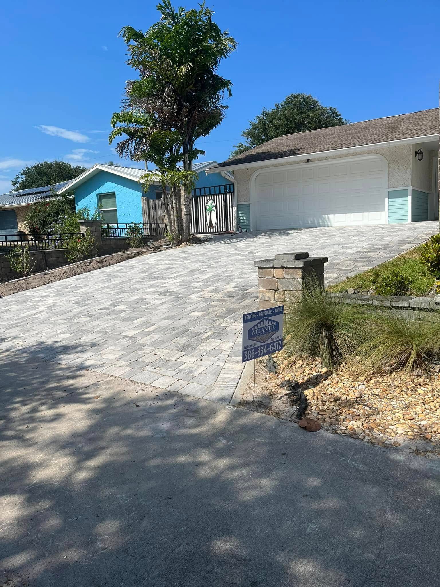 Driveway leading to a white garage and a blue house on a sunny day.