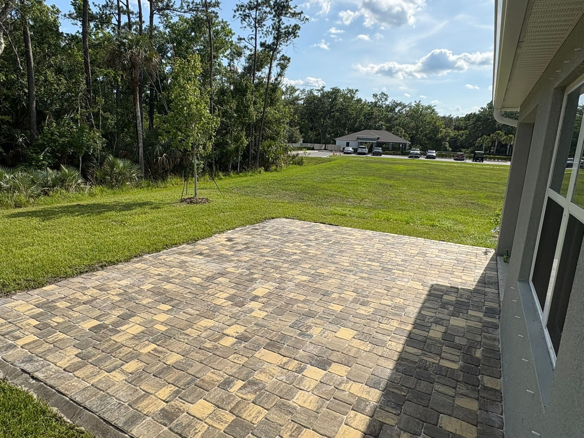 Brick patio next to a house, overlooking a grassy yard and trees.