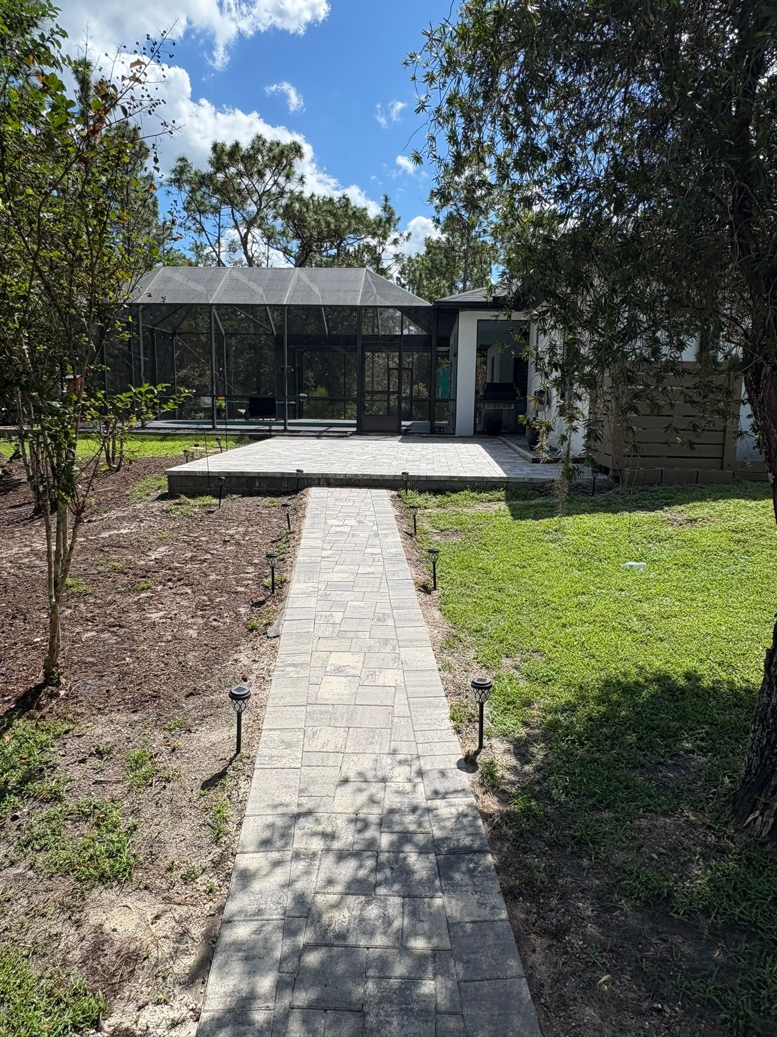 Stone walkway leading to a modern glass-front house surrounded by trees and greenery