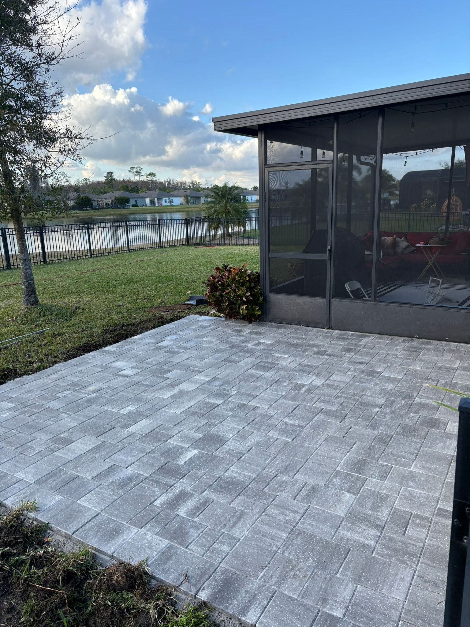 Patio by a lakeside yard with gray pavers, screened porch, and cloudy sky