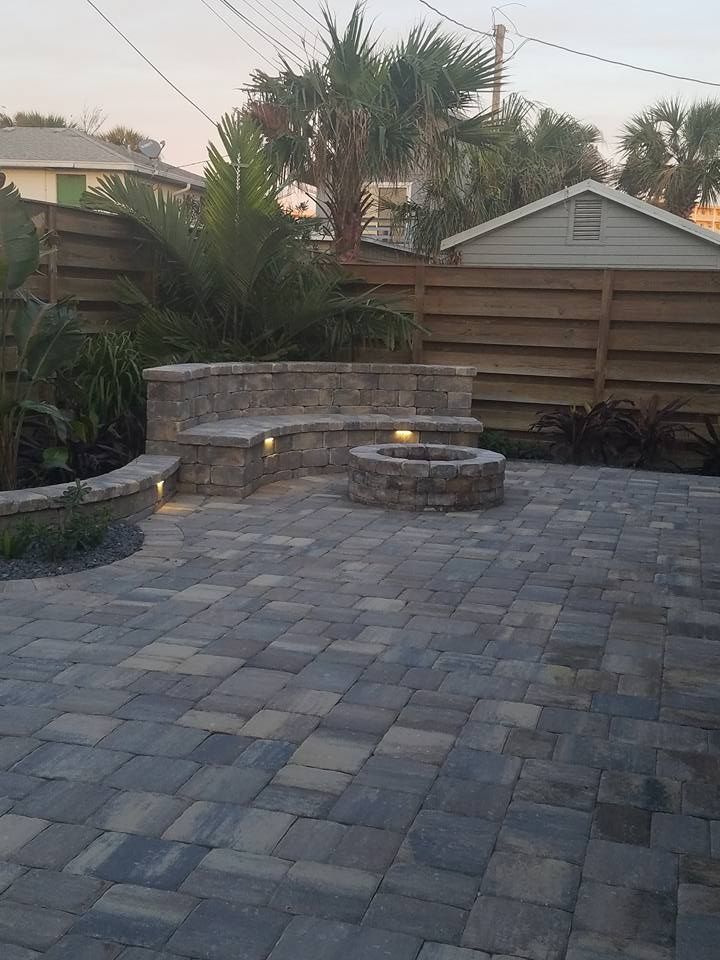 Stone patio with a built-in bench, fire pit, and wooden fence.