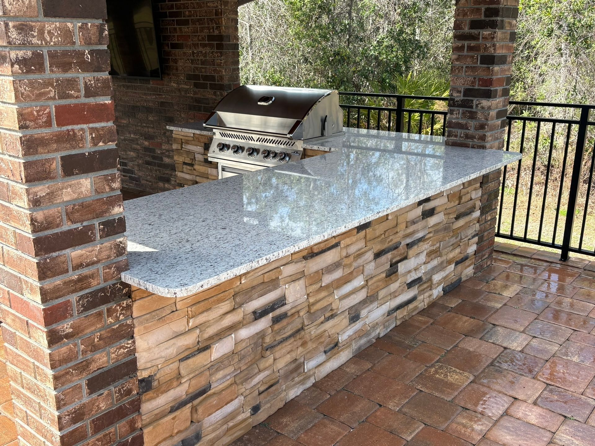 Outdoor brick patio with built-in stone grill and speckled granite countertop under a covered area