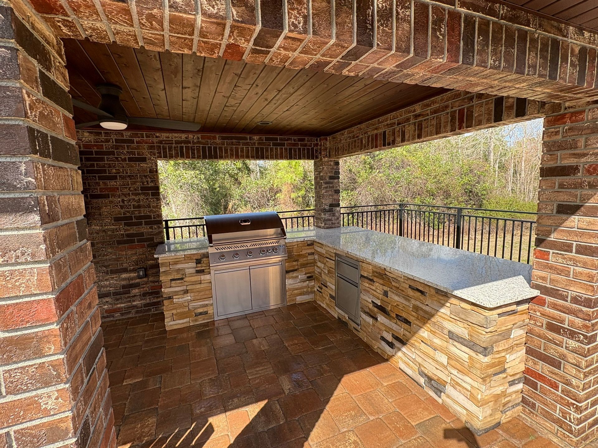 Brick outdoor kitchen with built-in grill and stone countertops under a covered patio.