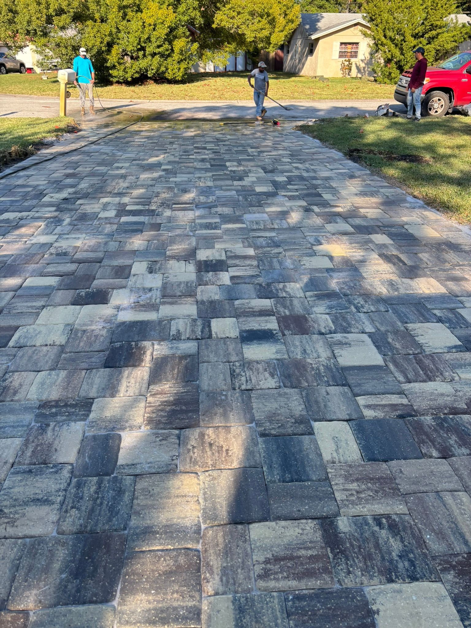 Newly paved checkerboard driveway with trees and a red truck in the background