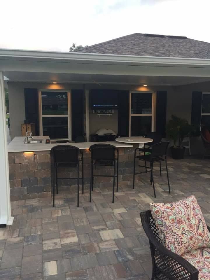 Outdoor kitchen with bar seating, stone patio, and overhead lighting.