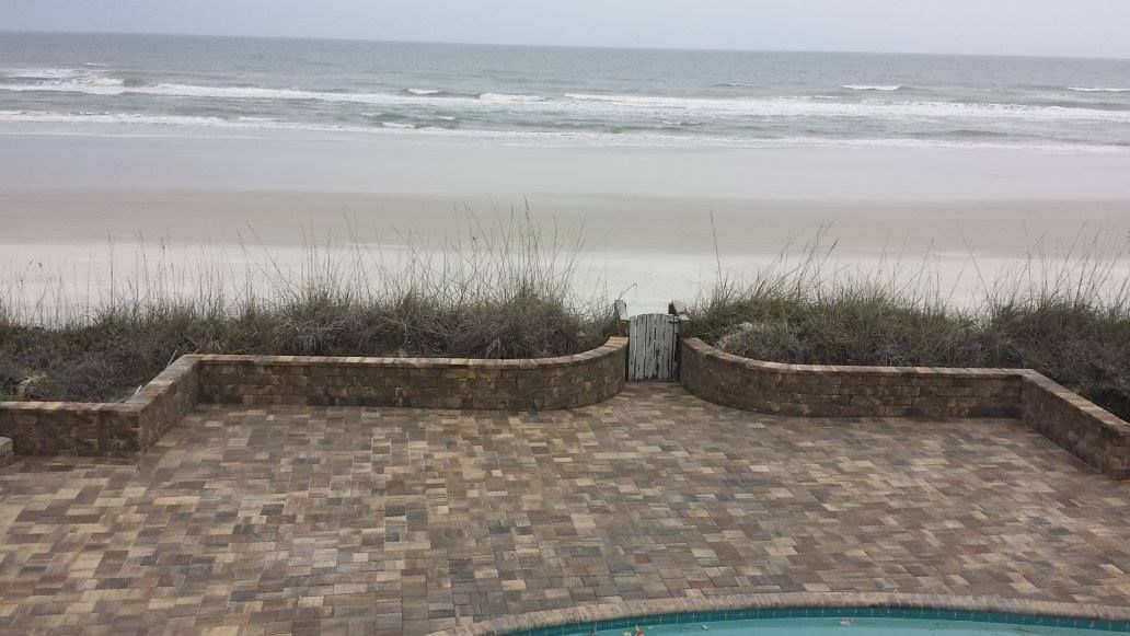 Beachfront patio with brick pavers, low wall, and ocean view.