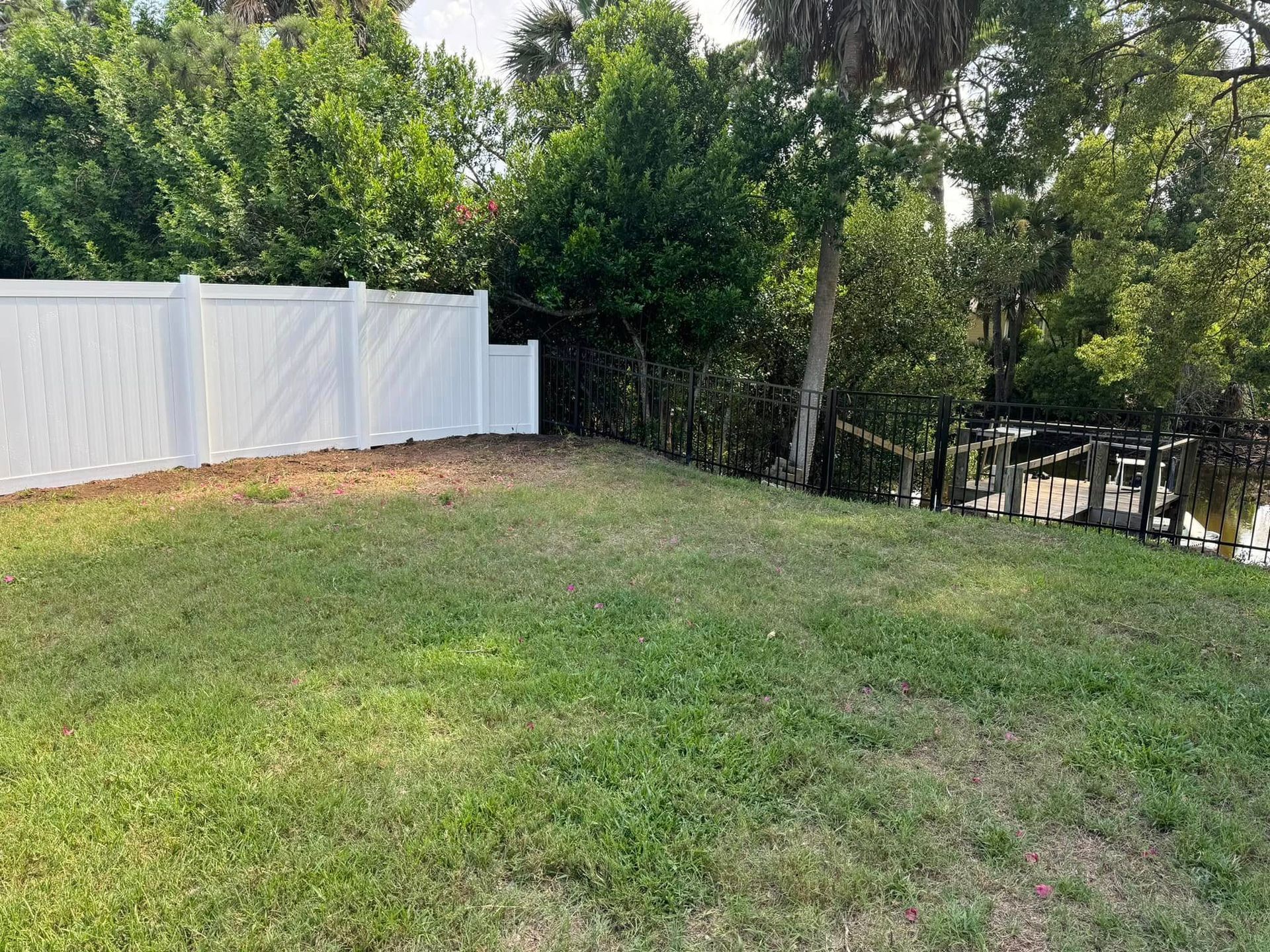 White fence bordering a grassy yard next to a waterway, with trees and docks visible.