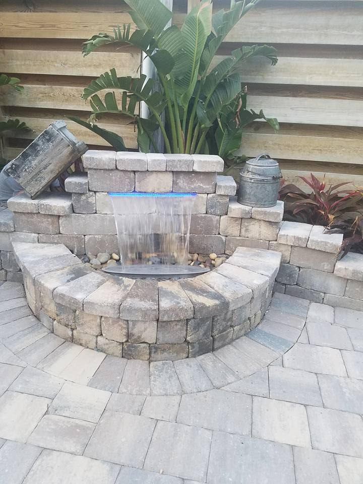 Water feature made of stone brick; water cascading down; plant in background.