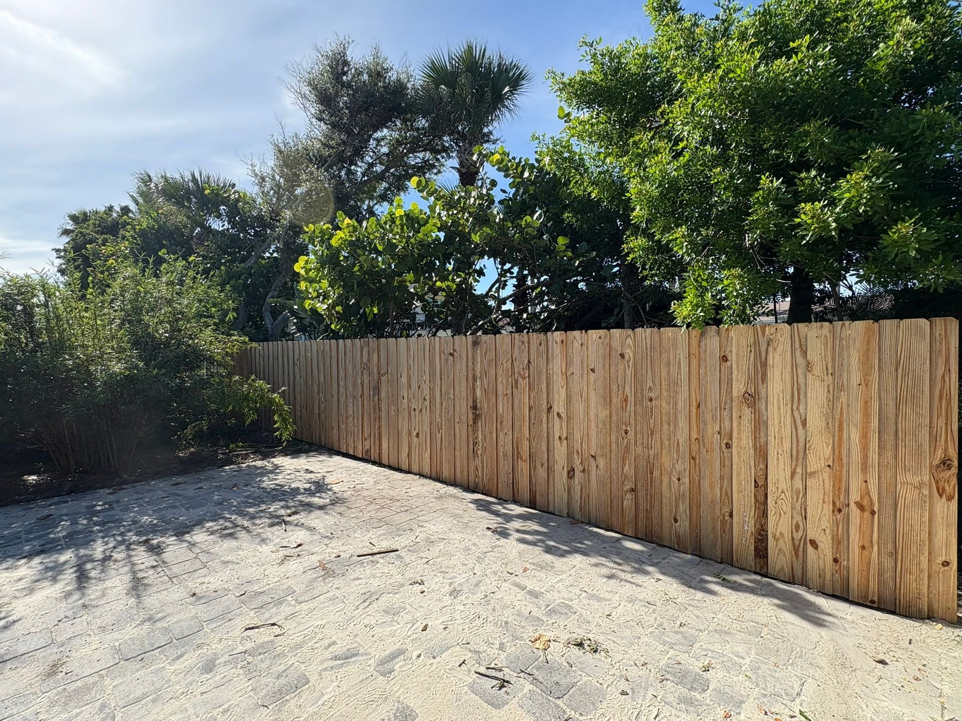 Wooden fence along a sandy area, with trees in background and bright sunlight.