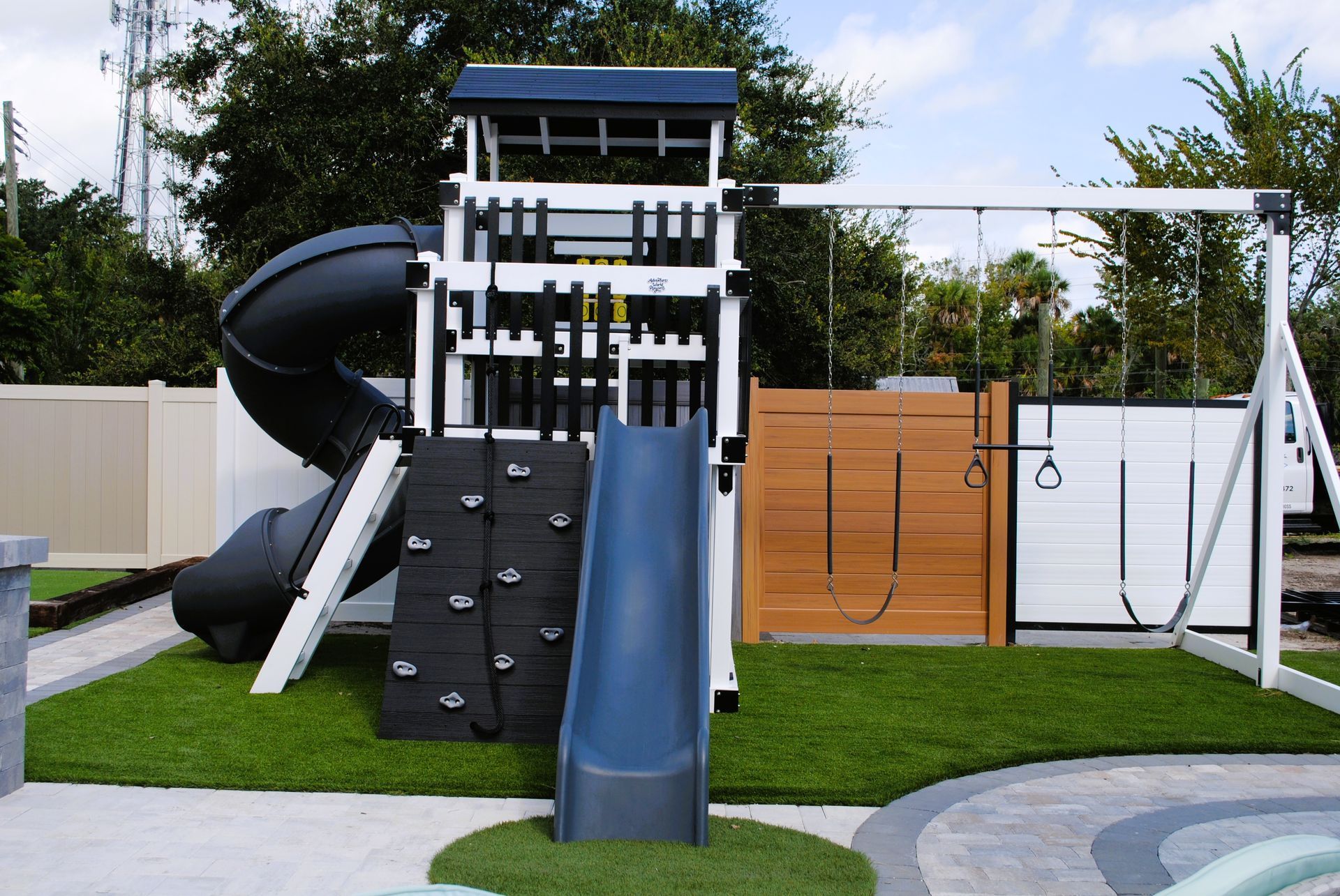 Playground with dark blue slide, climbing wall, swings, and wooden panels on green turf.