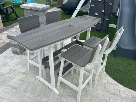 Gray outdoor dining table with four chairs on a paved patio in a yard
