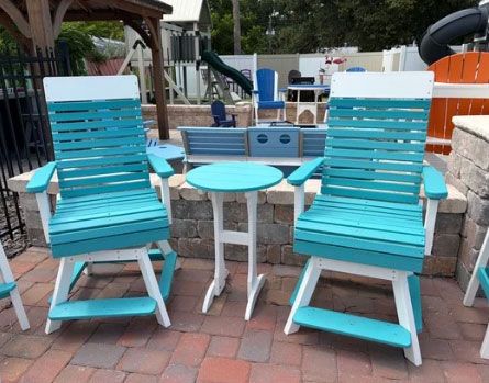 Two turquoise chairs with a small round table on a brick patio by a pool