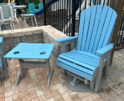 Blue chair and matching side table on a brick patio near a black fence.