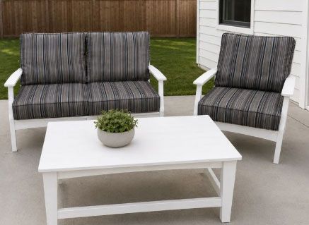 White patio loveseat and chair with striped cushions beside a white coffee table and potted plant outdoors