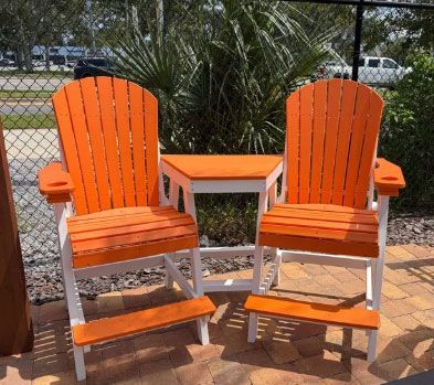 Two orange chairs with a small orange table on a patio by a fence and palm plants