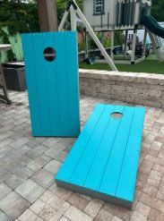 Turquoise outdoor corn hole set on a paved patio, with one board upright and one flat.