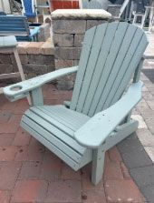 Light blue wooden Adirondack chair on a brick patio beside stacked stone blocks.