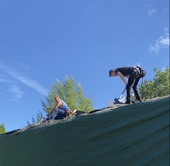 Two people on a sloped roof under a blue sky, one crouching and one sitting nearby.