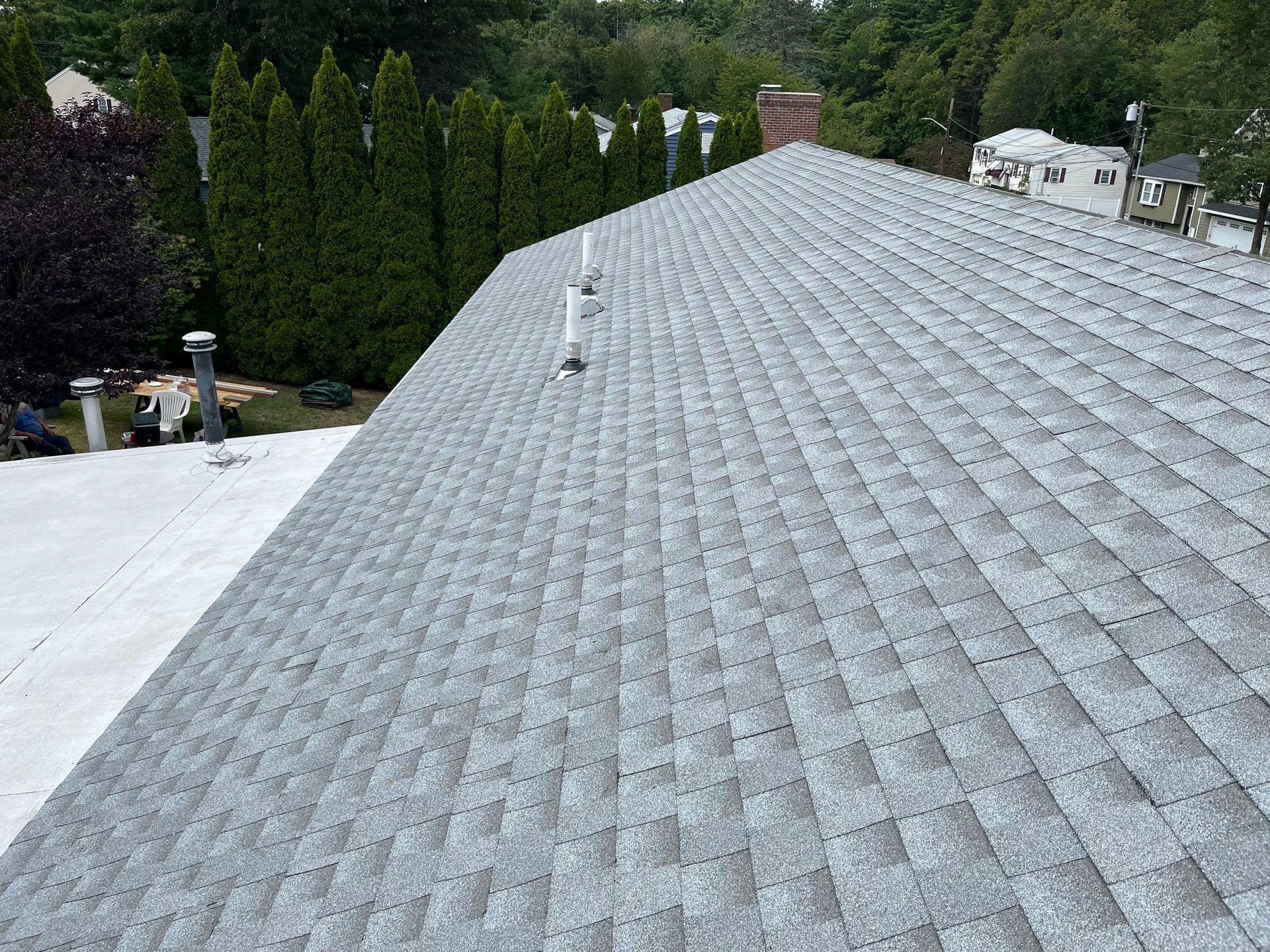 Gray shingled roof viewed from above, with trees and neighboring houses in the background