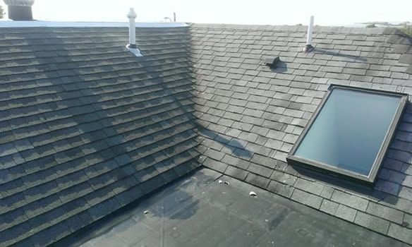Rooftop with gray shingles, a skylight, and a chimney under a cloudy sky
