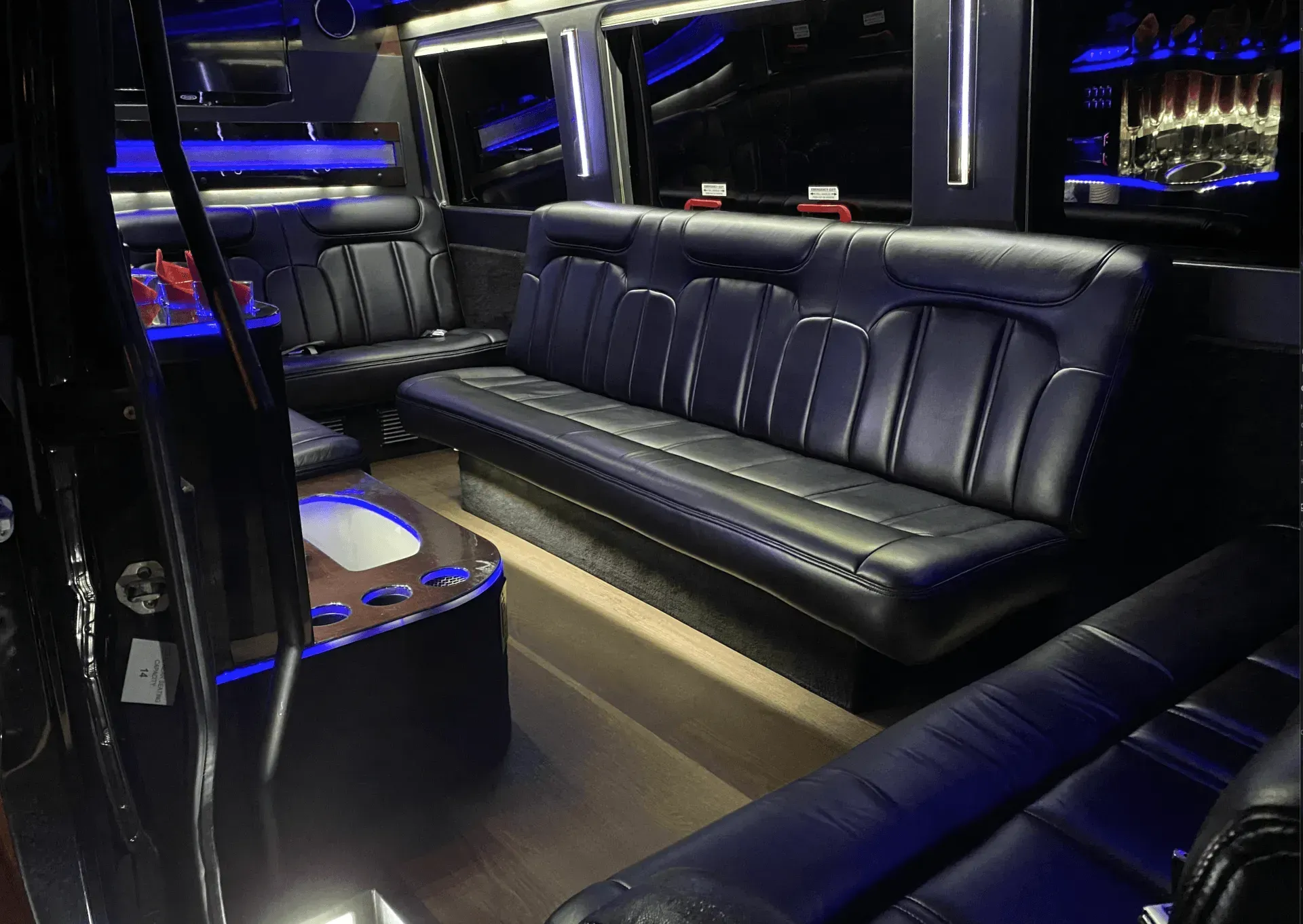 Interior of a black limo with leather seating, blue mood lighting, and a small bar.