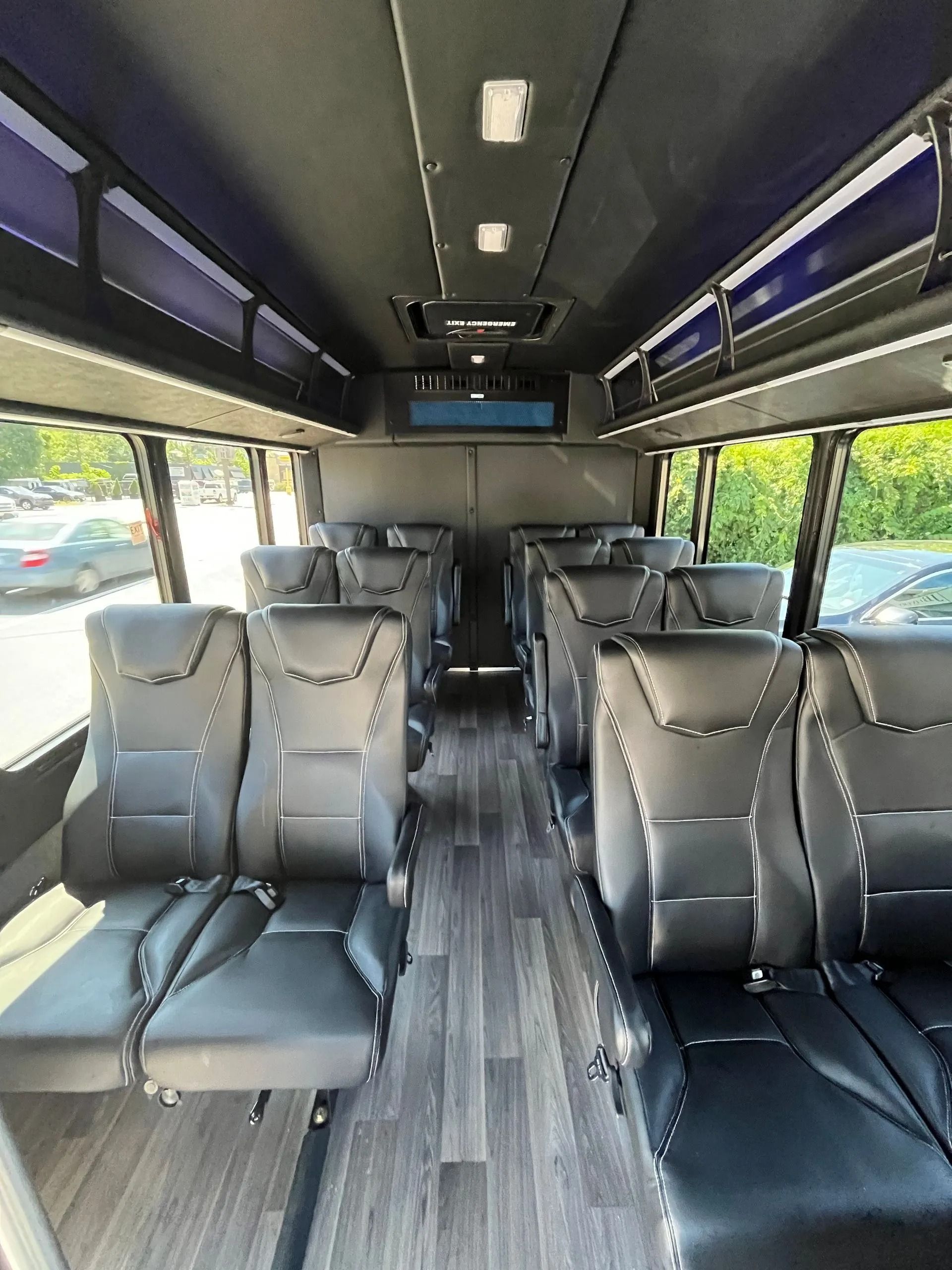 Interior of a bus with rows of black seats, grey floor, and windows.