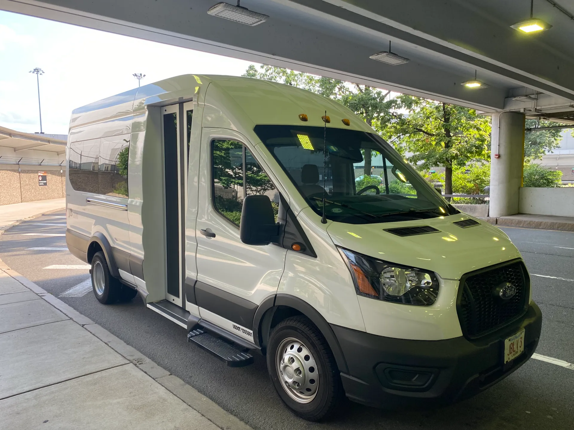 White passenger van parked under a covered area; open door with step; parked next to a curb.