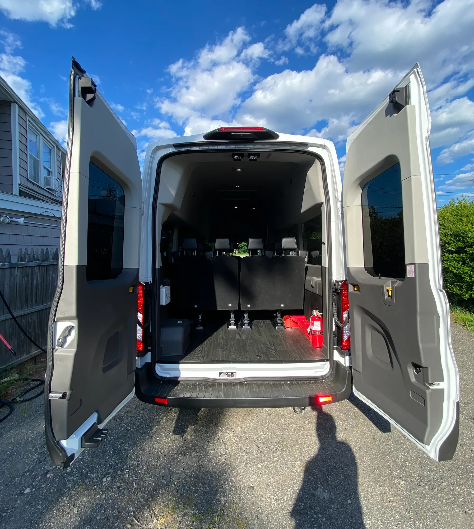 White van with open rear doors, interior visible. Black seating, red fire extinguisher, sunny outdoor setting.