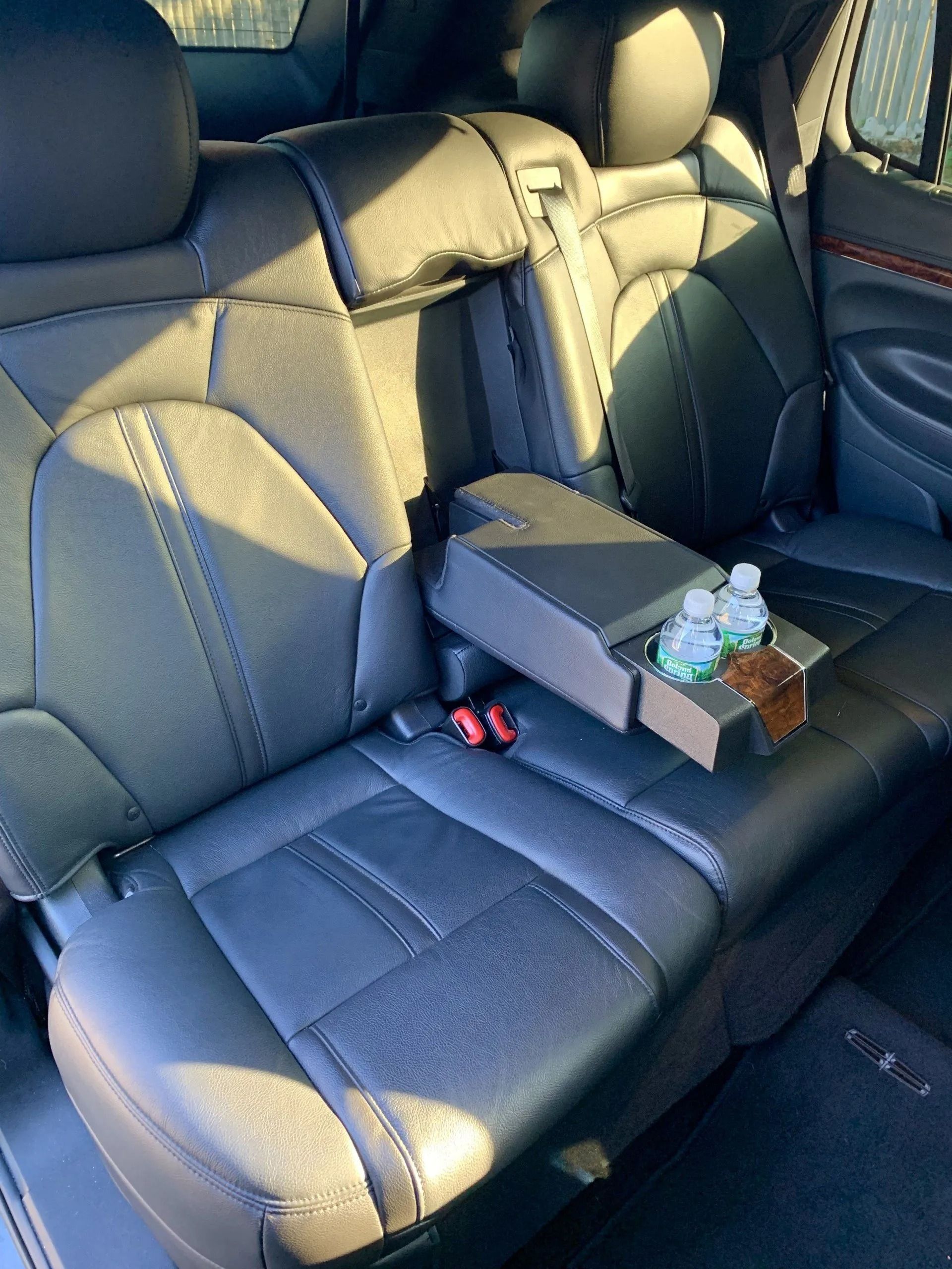 Black leather car back seats with armrest, containing two water bottles and snacks.