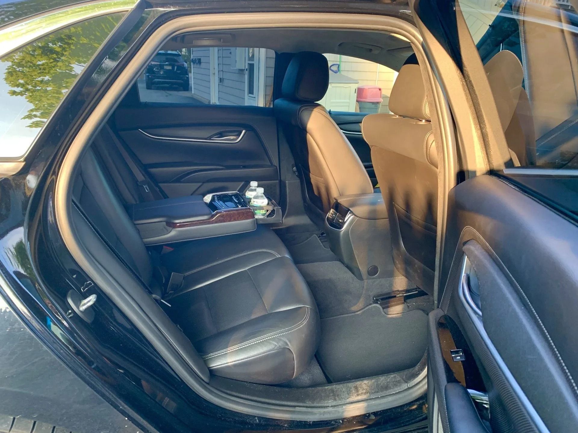 Black car's open backseat with leather seats, a center console, and a water bottle. Sunlight streams through the windows.