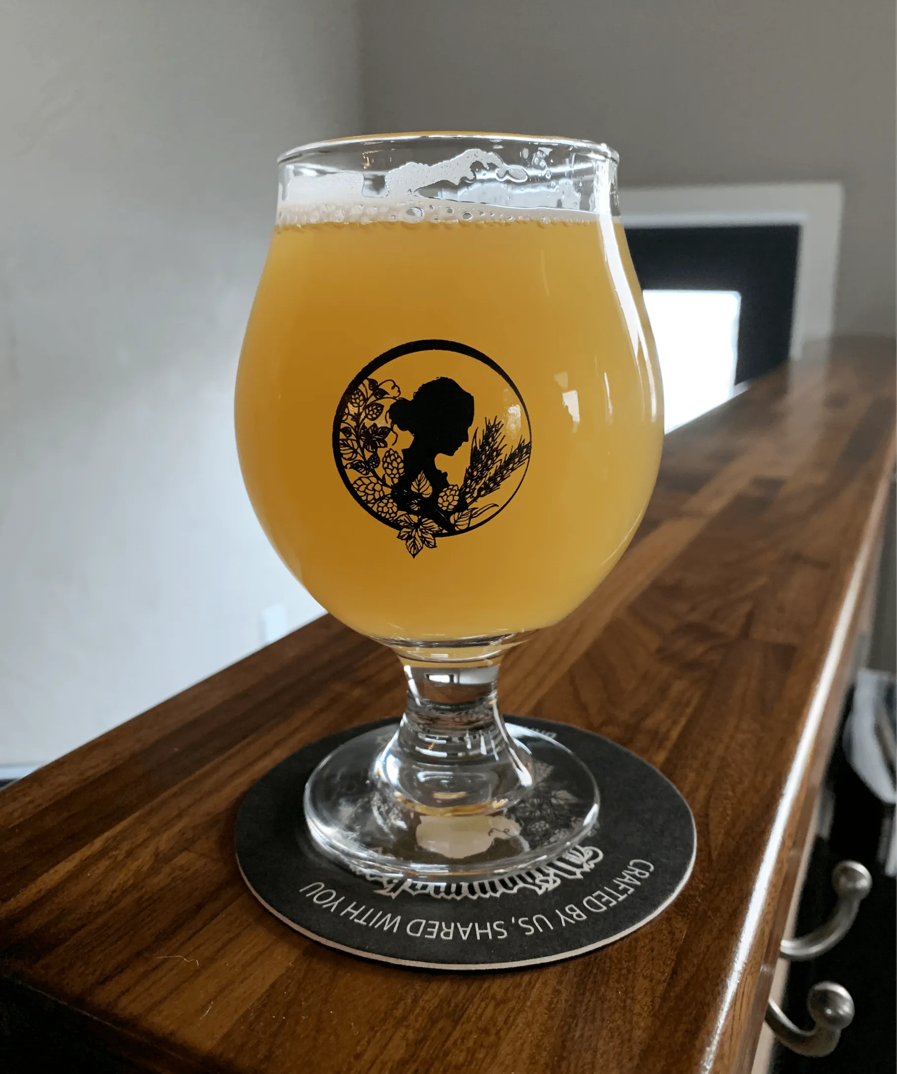 A glass of hazy yellow beer on a coaster atop a wooden surface.