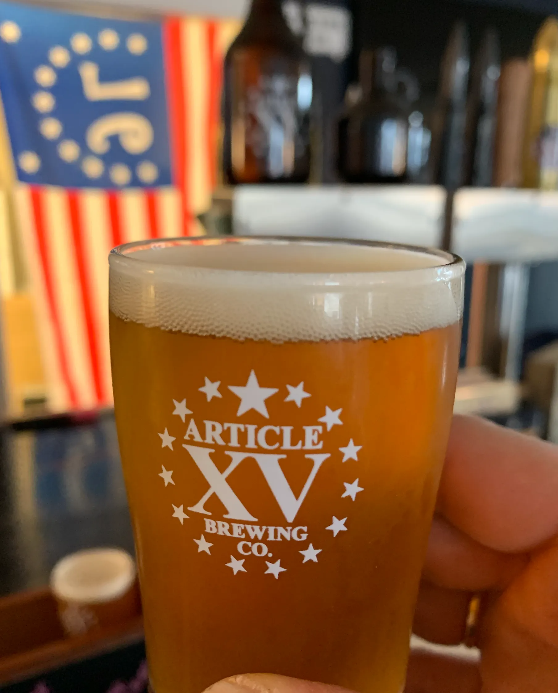 Glass of beer with the Article XV Brewing Co. logo, American flag in the background.