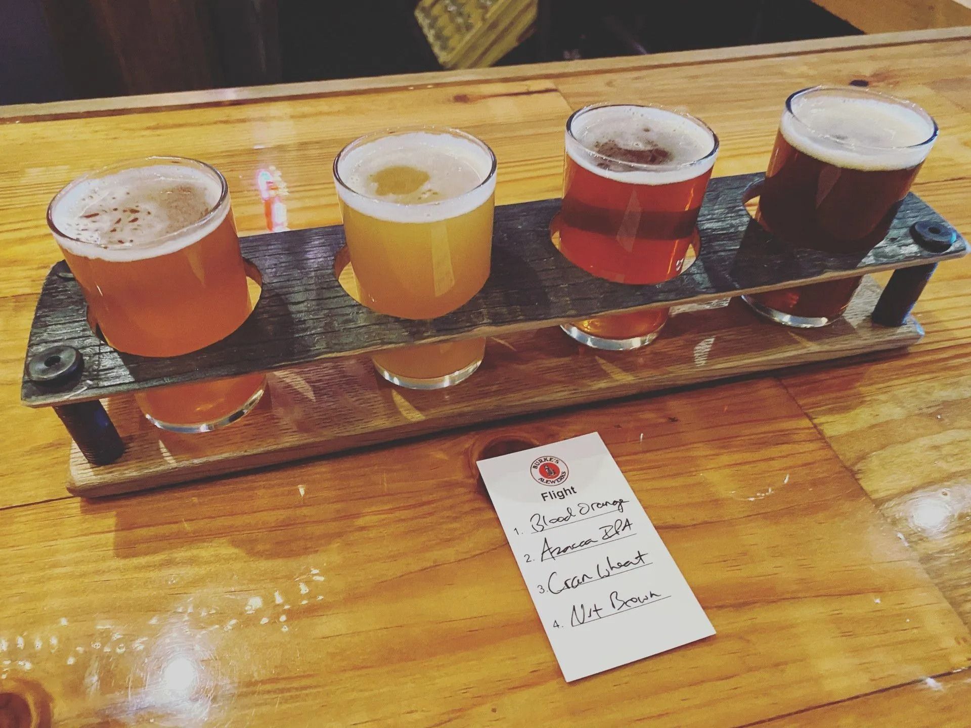 Flight of four beers in different colors on a wooden tray, with a handwritten label.