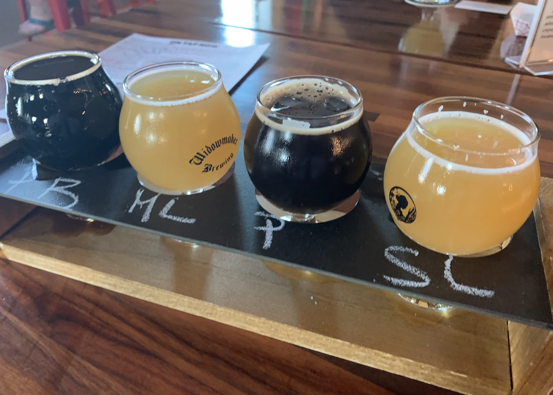 A beer flight with four different beers in small, round glasses on a wooden table.