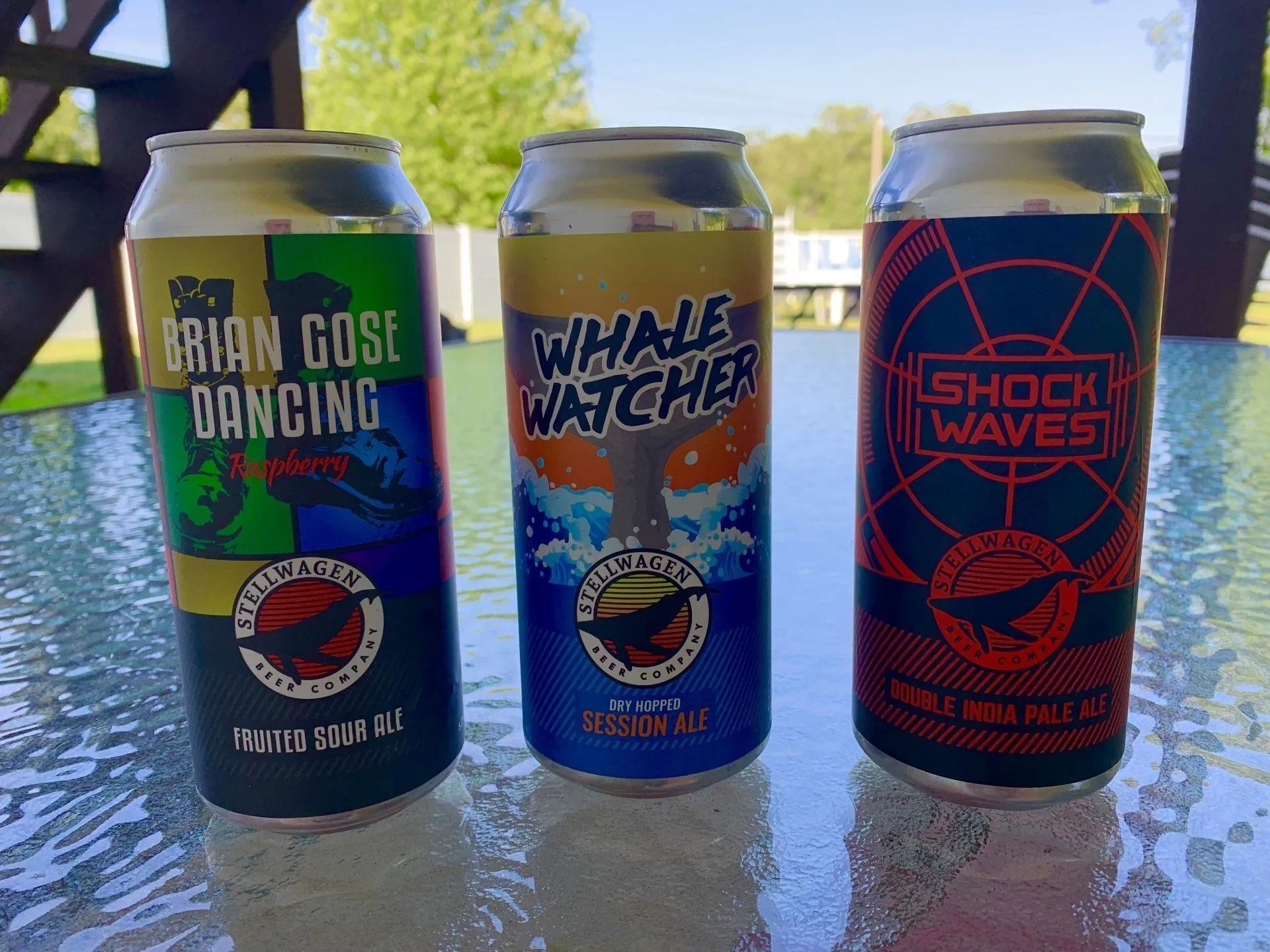 Three colorful beer cans on a glass table outdoors: