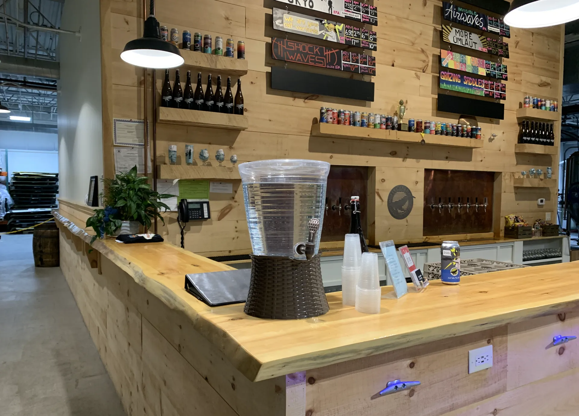A wooden bar inside a brewery with beer taps, bottles, and water dispenser.