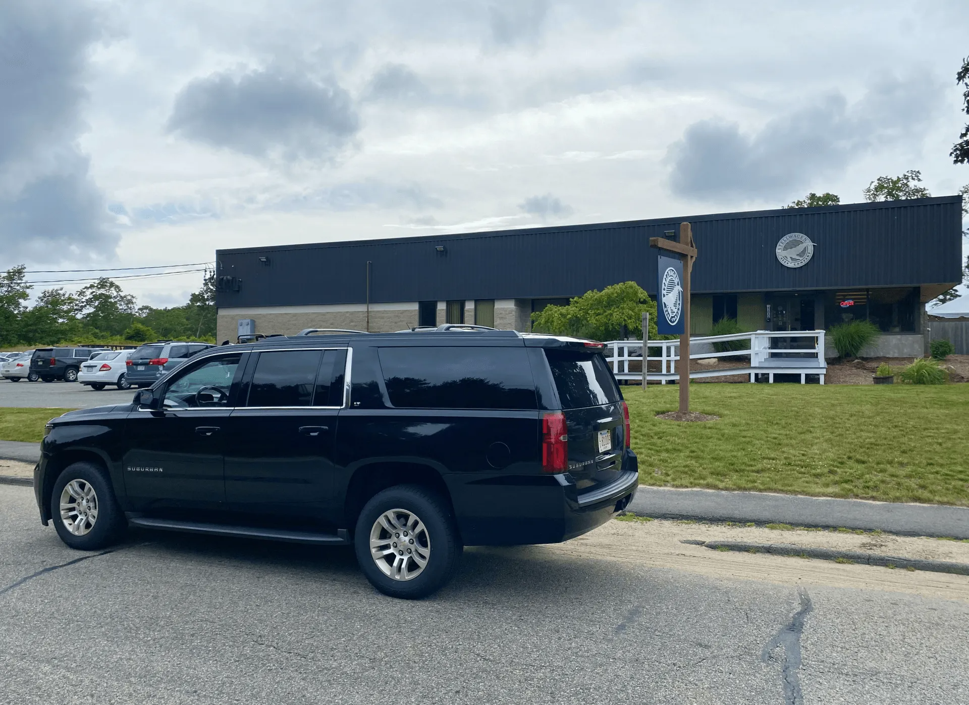 Black SUV parked in front of a dark building with a sign. Cloudy sky and parking lot visible.