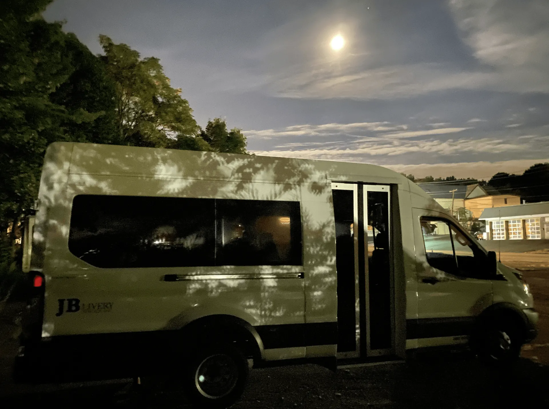 A white van parked at night under a full moon, shadowed by trees.