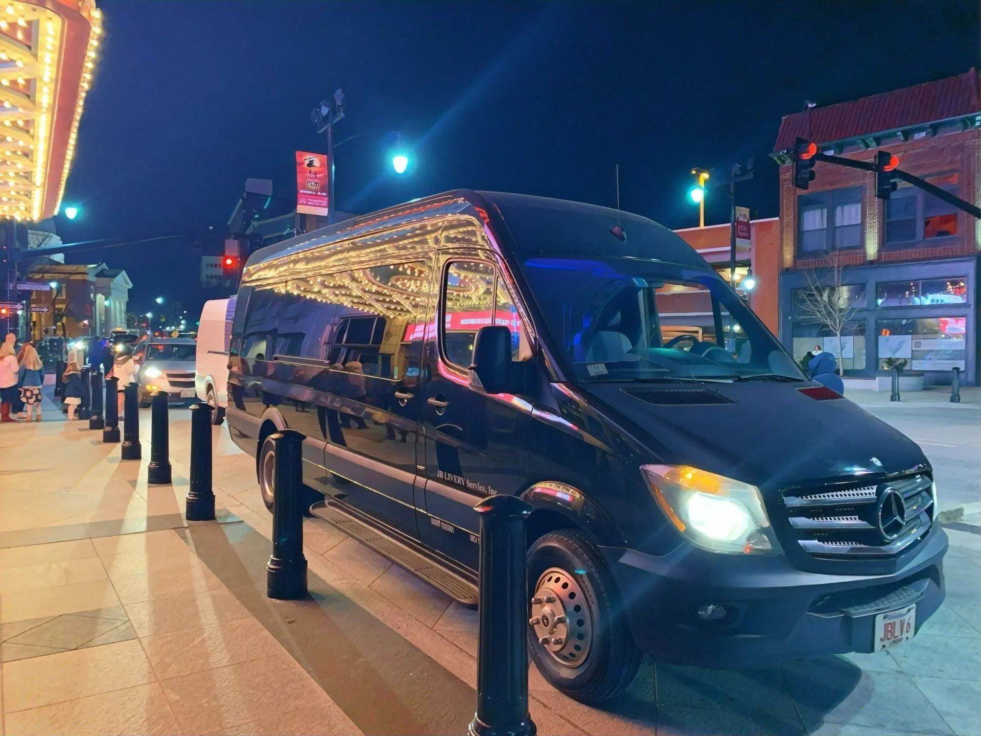 Black Mercedes Sprinter van parked on a city street at night with buildings and lights.
