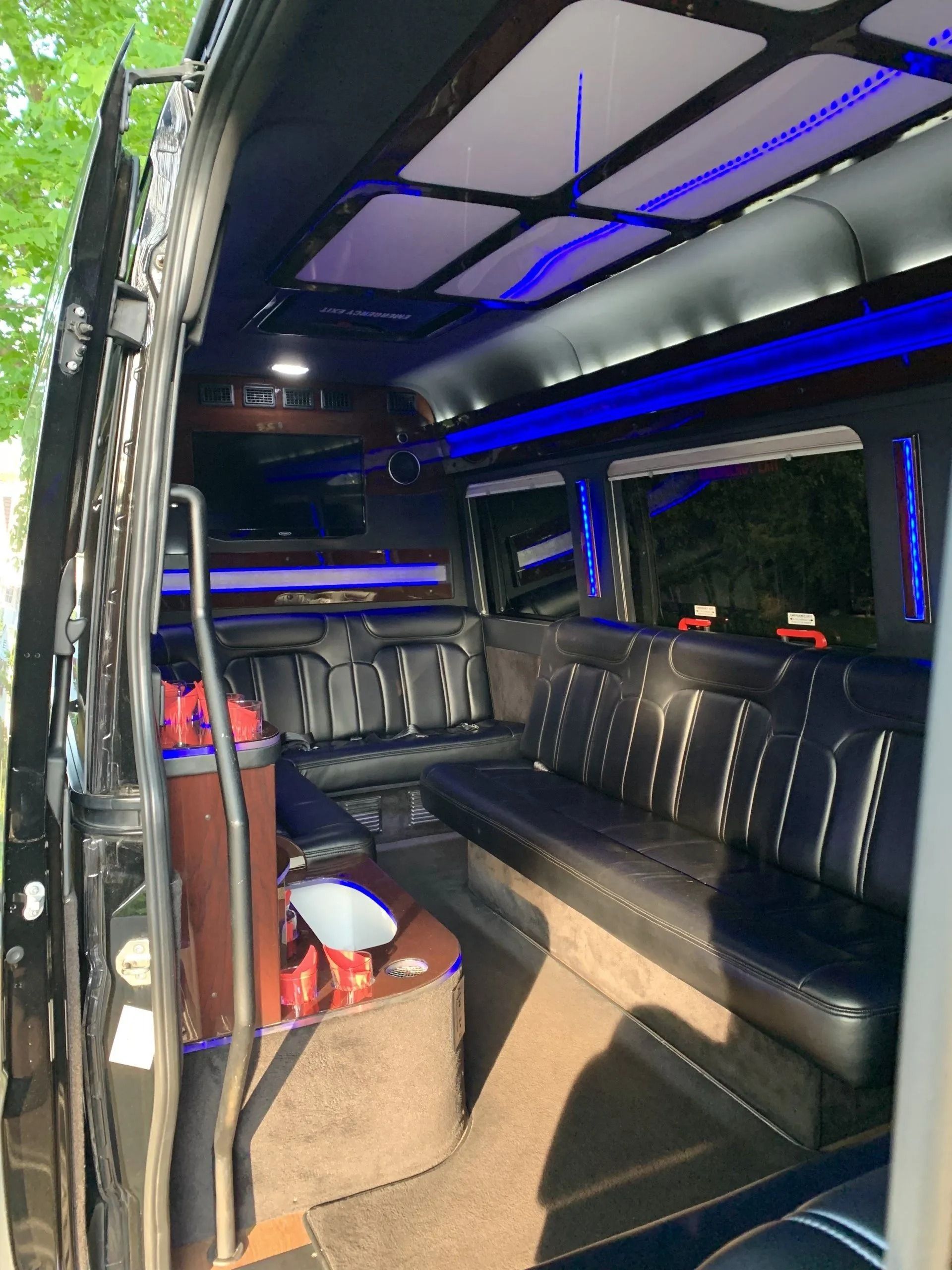 Interior of a black luxury van with black leather seating, blue lights, and a wet bar.